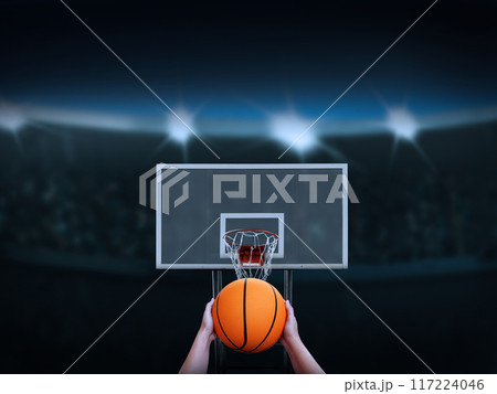 Hand holding a basketball about to shoot it into the basketball backboard There is an amphitheater in the background. 117224046