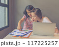 Two young women working with laptop and paperwork in discussion 117225257