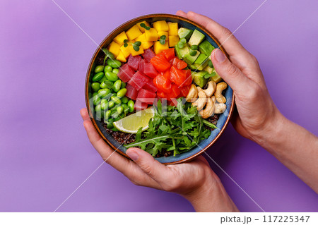 Poke bowl with salmon and tuna in hand on a purple background Poke bowl with salmon and tuna in hand on a purple background 117225347