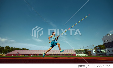 High jump training in progress, with a strong and focused pole vaulter in motion, running wit pole at outdoor stadium High jump training in progress, with a strong and focused pole vaulter in motion, running wit pole at outdoor stadium 117226862