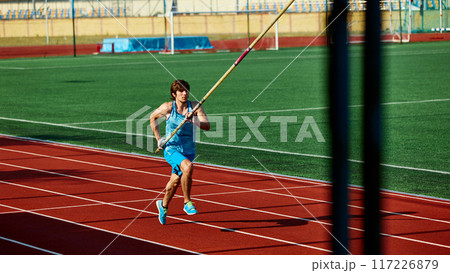 Motivated pole vaulter, muscularly young man in blue sportswear in motion with pole, practicing with precision and strength on track. Motivated pole vaulter, muscularly young man in blue sportswear in motion with pole, practicing with precision and strength on track. 117226879