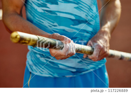 Determined pole athlete getting ready to conquer the bar, cropped image of male hands in chalk powder holding pole. Determined pole athlete getting ready to conquer the bar, cropped image of male hands in chalk powder holding pole. 117226889
