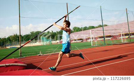 Determined pole athlete training hard, focusing on strength and technique, young man in blue uniform getting ready to jump with pole Determined pole athlete training hard, focusing on strength and technique, young man in blue uniform getting ready to jump with pole 117226895