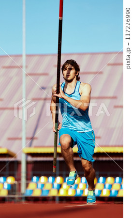 Motivated young man, pole jumping athlete in motion, practicing pole vaulting, aiming to reach new heights. Outdoor stadium 117226990