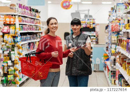 The sales consultant offers the buyer a new product in the supermarket. Two happy young Caucasian women. Concept of shopping, business and trade The sales consultant offers the buyer a new product in the supermarket. Two happy young Caucasian women. Concept of shopping, business and trade 117227654