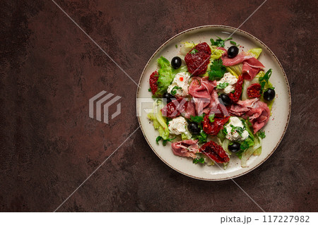 salad with dried tomatoes, prosciutto, soft cheese, olives, homemade, top view, 117227982