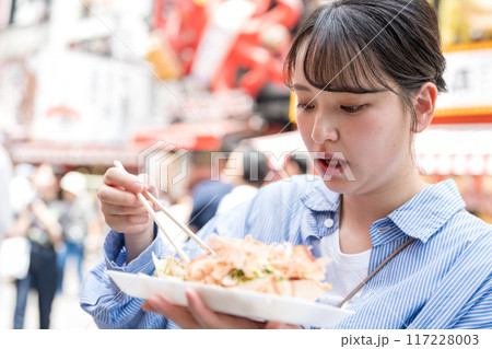 明るい屋外でたこ焼きを食べる女性｜大阪府大阪市道頓堀にて 117228003
