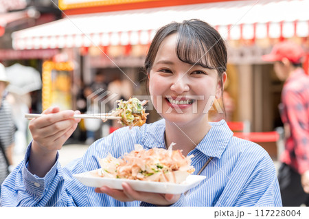 明るい屋外でたこ焼きを食べる女性｜大阪府大阪市道頓堀にて 117228004