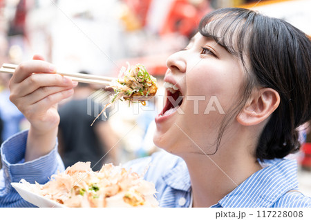 明るい屋外でたこ焼きを食べる女性｜大阪府大阪市道頓堀にて 117228008