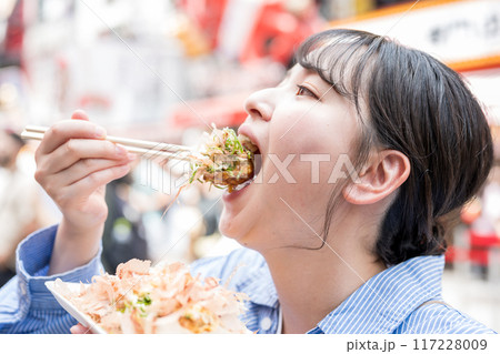 明るい屋外でたこ焼きを食べる女性｜大阪府大阪市道頓堀にて 117228009