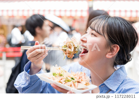 明るい屋外でたこ焼きを食べる女性｜大阪府大阪市道頓堀にて 117228011