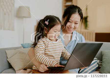 Asian mother and her little daughter smiling while playing computer game together in nursery 117228033