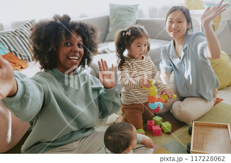 African American blogger smiling and waving while taking selfie with her Asian friend and her daughter during playing, bloggers son interested in bricks African American blogger smiling and waving while taking selfie with her Asian friend and her daughter during playing, bloggers son interested in bricks 117228062