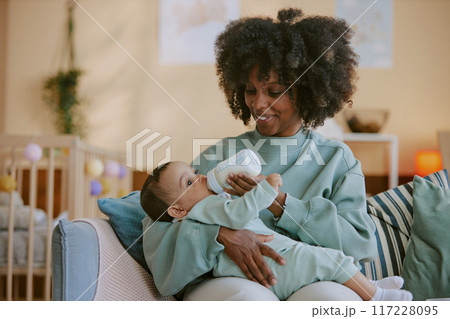 African American mother holding her son and feeding him while he looking around nursery and eating African American mother holding her son and feeding him while he looking around nursery and eating 117228095