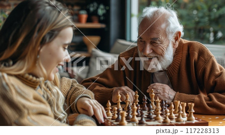 Adult granddaughter and elderly grandfather playing chess in a cozy living room. Grandparents day 117228313