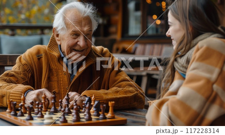 Adult granddaughter and elderly grandfather playing chess in a cozy living room. Grandparents day 117228314