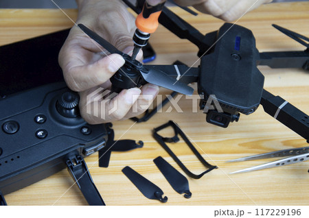 Professional mechanic repairing a drone with a small screwdriver on the table with various tools in modern workshop 117229196