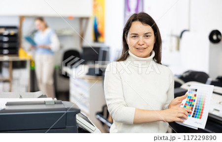 Portrait of positive woman printing office worker with colour test page Portrait of positive woman printing office worker with colour test page 117229890