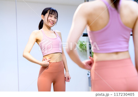 スポーツジムでお腹を気にする若い笑顔の女性　ダイエット　パーソナルジム　筋トレ女子　 117230405