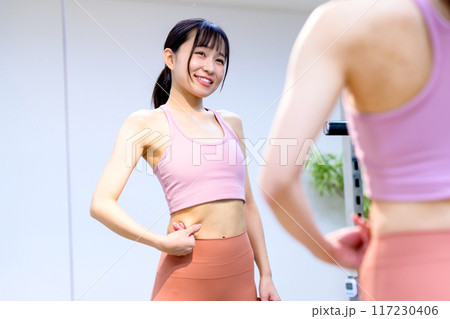 スポーツジムでお腹を気にする若い笑顔の女性　ダイエット　パーソナルジム　筋トレ女子　トリミングアップ 117230406