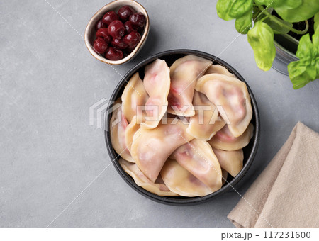 Dumplings with cherry. Delicious vegetarian vareniki with berries in a bowl on a gray background Dumplings with cherry. Delicious vegetarian vareniki with berries in a bowl on a gray background 117231600