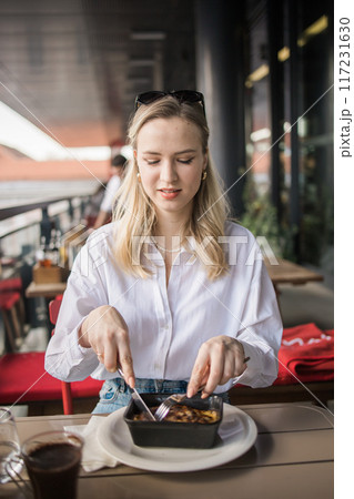 Blonde gen z woman eating lasagna in the cafe on break. Gen z girl spend time in restaurant 117231630
