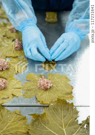 A woman in gloves prepares dolma - meat with vegetables wrapped in grape leaves.  117231641