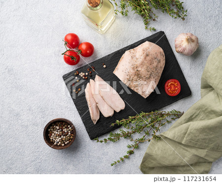 Baked chicken breast cut into pieces on a black slate board on a light background with fresh tomato Baked chicken breast cut into pieces on a black slate board on a light background with fresh tomato 117231654