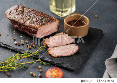 Grilled BBQ duck breast in marinade and spices with sauce on a slate board with fresh herbs Grilled BBQ duck breast in marinade and spices with sauce on a slate board with fresh herbs 117231678