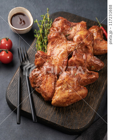 Spicy grilled chicken wings BBQ with sauce on a wooden plate with tomato and herb  117231688