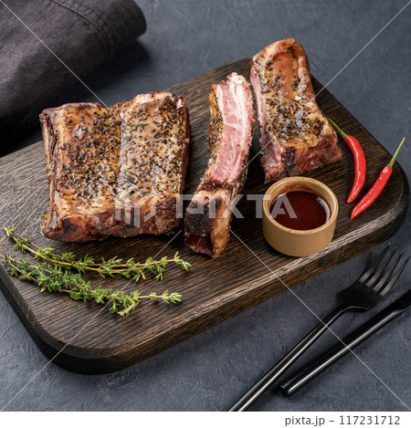 Grilled beef ribs with bbq sauce, chili pepper and fresh herb on a wooden board on a dark background Grilled beef ribs with bbq sauce, chili pepper and fresh herb on a wooden board on a dark background 117231712
