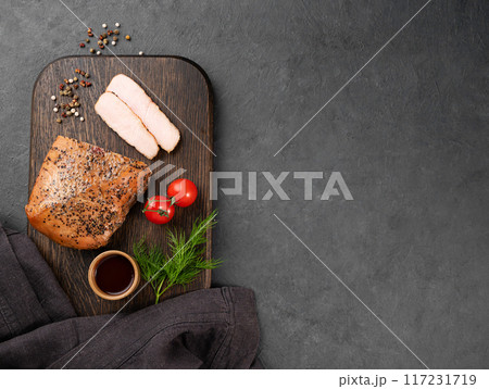 Grilled BBQ turkey breast slices in marinade with fresh herbs and vegetables on a dark background. 117231719