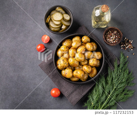Fresh young roasted baby potatoes in a black pan with tomatoes and herbs on a dark  background. 117232153