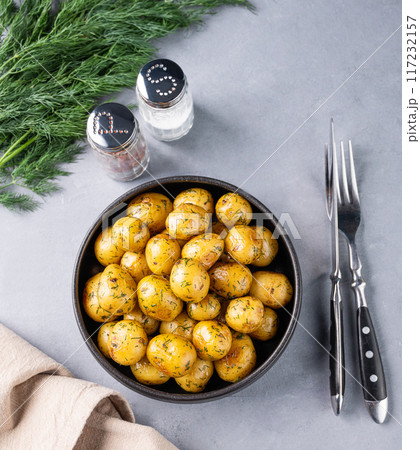 Young roasted baby potatoes in a black  pan with salt and herb on a blue background. 117232157