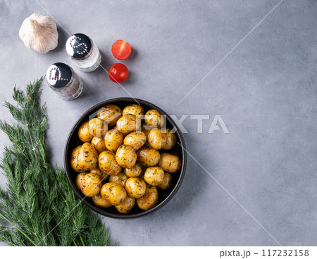 Young roasted baby potatoes in a black pan with tomatoes, garlic and herb on a blue background. Young roasted baby potatoes in a black pan with tomatoes, garlic and herb on a blue background. 117232158