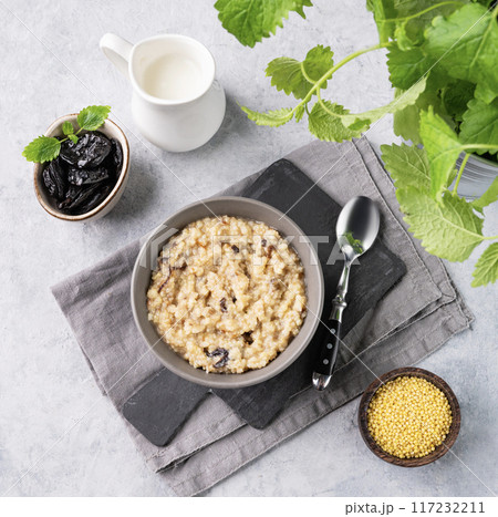 Couscous or millet porridge with prunes in bowl with milk on a blue background. Couscous or millet porridge with prunes in bowl with milk on a blue background. 117232211