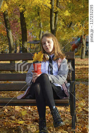 a girl sits on a bench in an autumn park 117232295