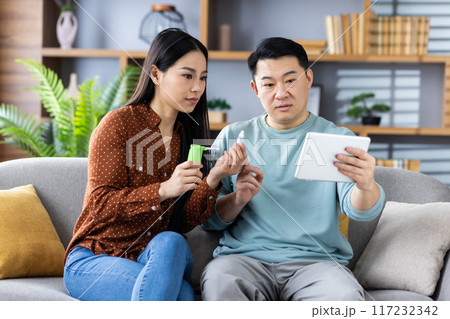 Asian family having online consultation with doctor through video call on tablet. Two people discussing health issues, showing medication and following doctor's advice. 117232342