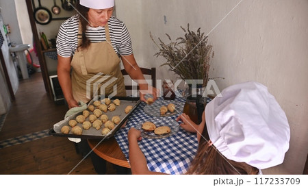 A mother and daughter spend quality time baking croissants together in a cozy kitchen. The little girl thoughtfully arranges baked goods while learning the art of cooking. A mother and daughter spend quality time baking croissants together in a cozy kitchen. The little girl thoughtfully arranges baked goods while learning the art of cooking. 117233709