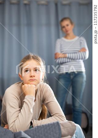 Sad female and daughter sitting at sofa and having quarrel 117235792