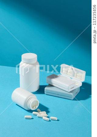 High angle shot photography at the baby blue table top, displaying an unbranded white medicine jar, white tablet spilled out and pill boxes. Blank space for designing 117235856