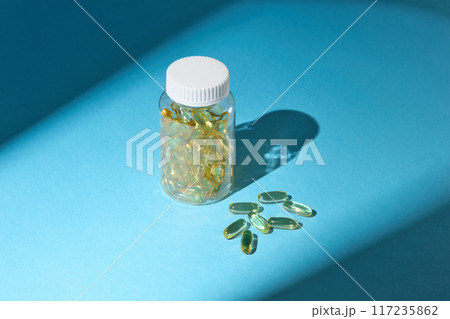The transparent supplement bottle isolated on blue background, next to some flat lay vitamin supplement capsule. The photo was taken from above view with blank space for promotional 117235862