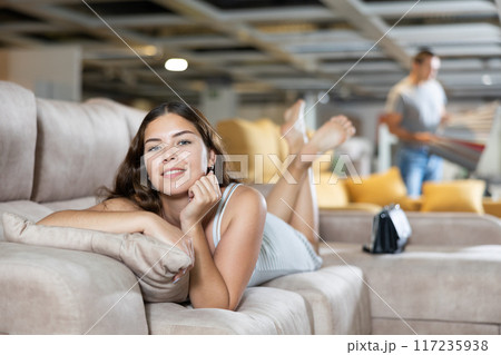 On sofa girl is lying on stomach with chin propped up in hands in furniture store 117235938