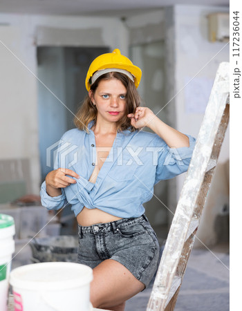 Sexy woman in denim shirt and shorts next to a stepladder in room being renovated 117236044