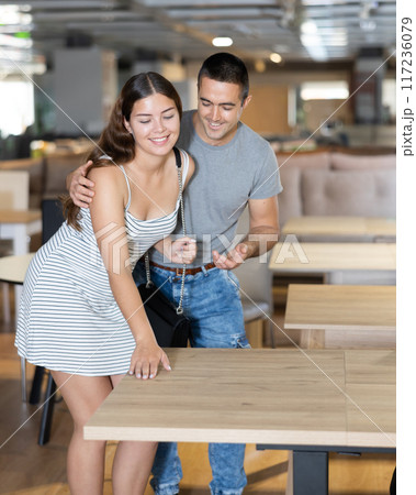 Husband and wife together choose and buy a modern wooden table in furniture store 117236079