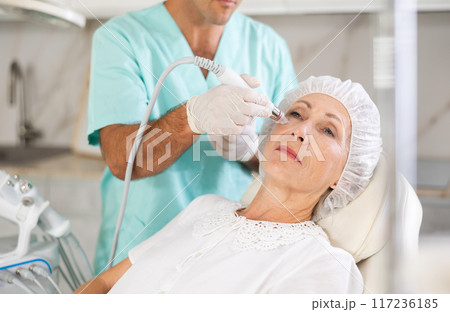 Male dermatologist performing cosmetology procedure for elderly woman, RF lifting and deep hydration for facial skin therapy Male dermatologist performing cosmetology procedure for elderly woman, RF lifting and deep hydration for facial skin therapy 117236185