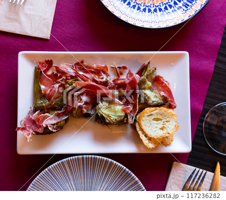 Dish of fried artichoke flowers and slices of ham is served on plate 117236282