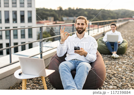 Remote work on rooftop with man using phone and laptop Remote work on rooftop with man using phone and laptop 117239884
