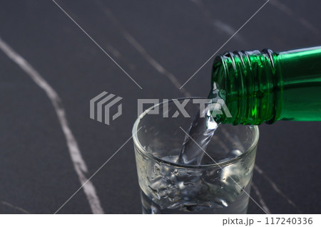 韓国の伝統的な蒸留酒、よく冷えた韓国焼酎(ソジュ)をグラスに注ぐ 韓国の伝統的な蒸留酒、よく冷えた韓国焼酎(ソジュ)をグラスに注ぐ 117240336