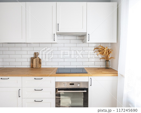 Cozy white kitchen with wooden countertop, flower and cutting boards in a minimalist interior Cozy white kitchen with wooden countertop, flower and cutting boards in a minimalist interior 117245690